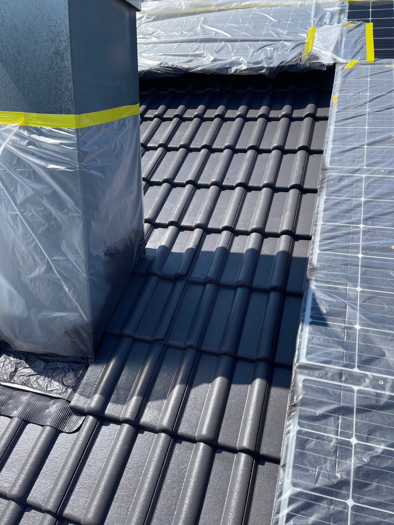 Dachbeschichtung Detail – frisch beschichtete anthrazitfarbene Ziegel am Kamin